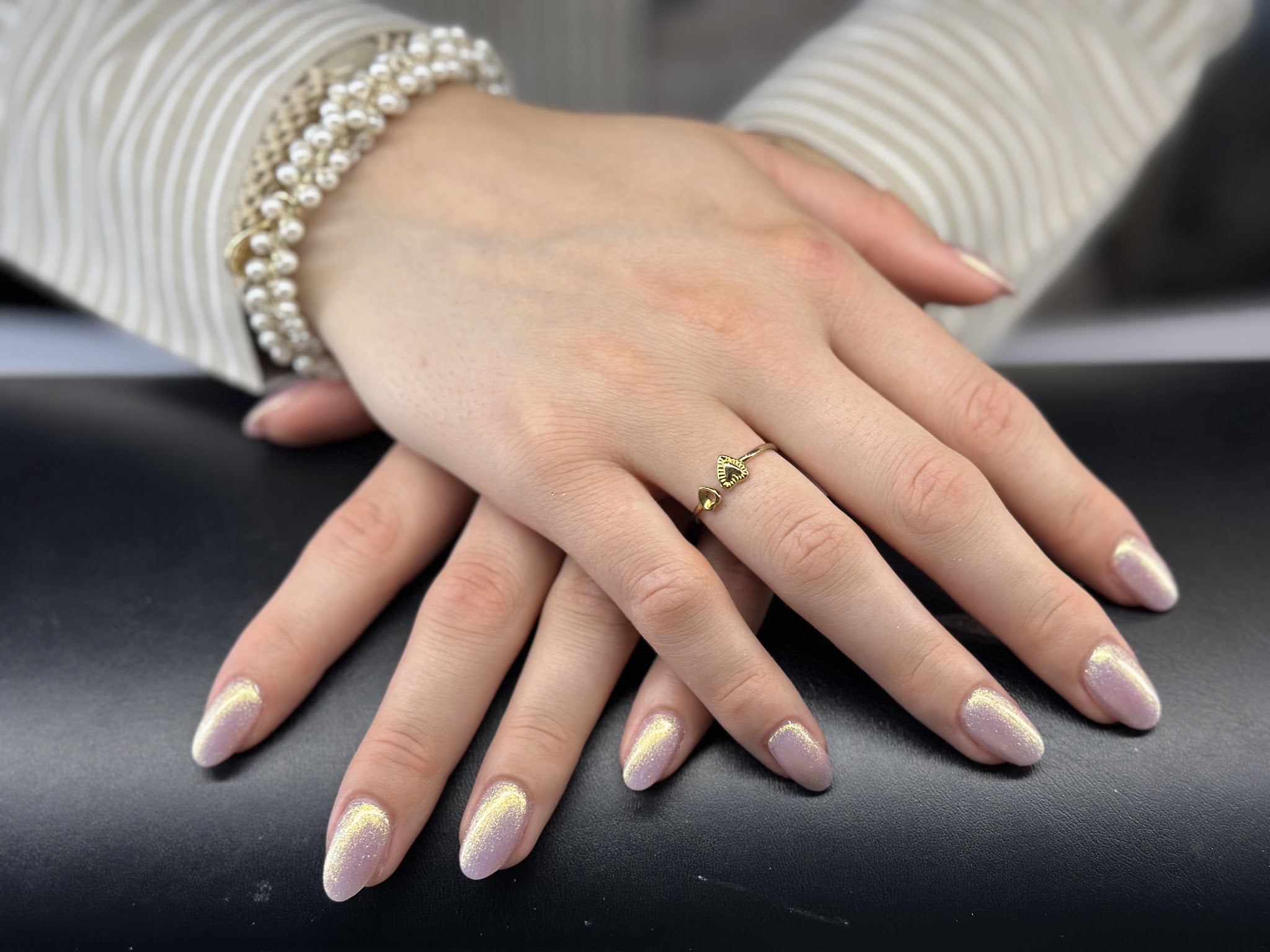 Amandelvormige nagels met parelmoer en chroomglans, handen op een zwarte armleuning